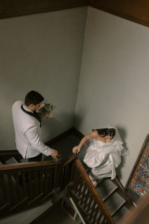 Wedding couple descending vintage wooden staircase in dramatic lighting.