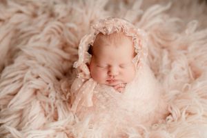 Peaceful sleeping newborn wrapped in pink lace on textured fur backdrop.