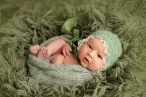 Newborn baby wearing mint green bonnet on textured green blanket.