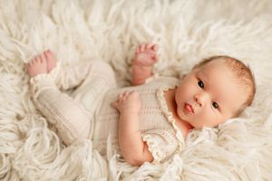 Baby in white knit outfit lying on plush white fur blanket.