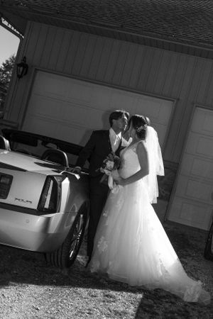 Black and white photo of bride and groom kissing next to car after wedding ceremony.