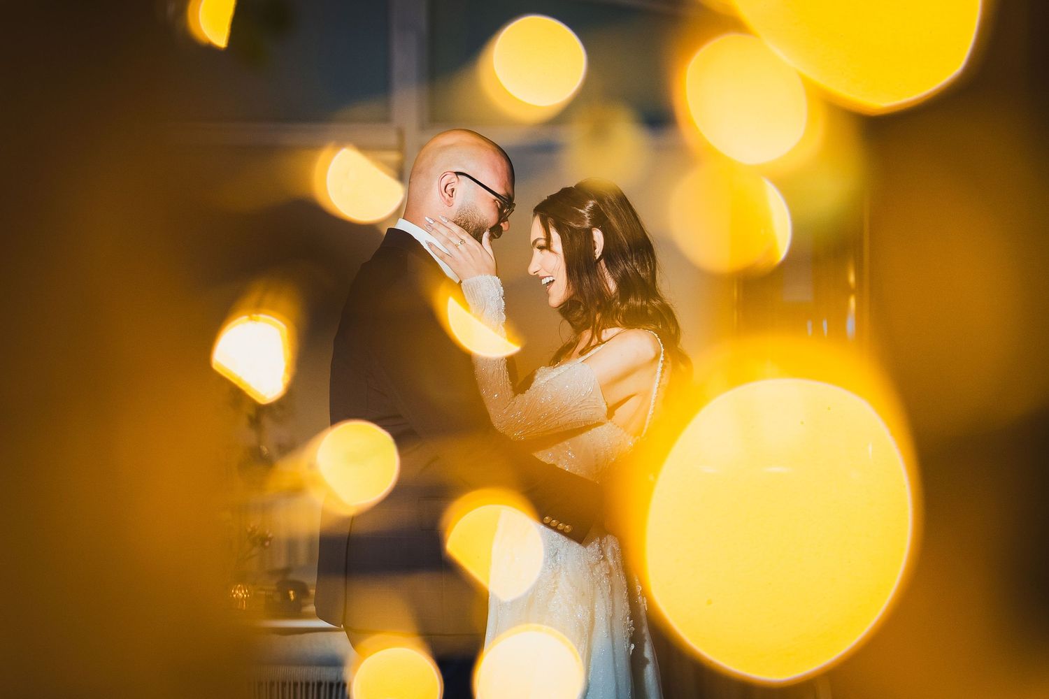 Couple dancing at a wedding reception with soft golden bokeh lights creating a romantic atmosphere.
