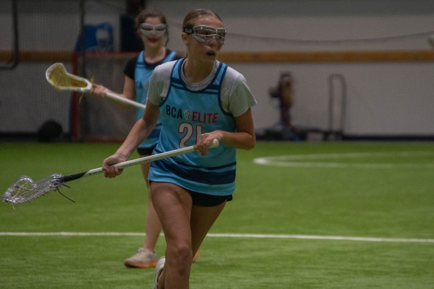 Player carries lacrosse stick while running during indoor practice.