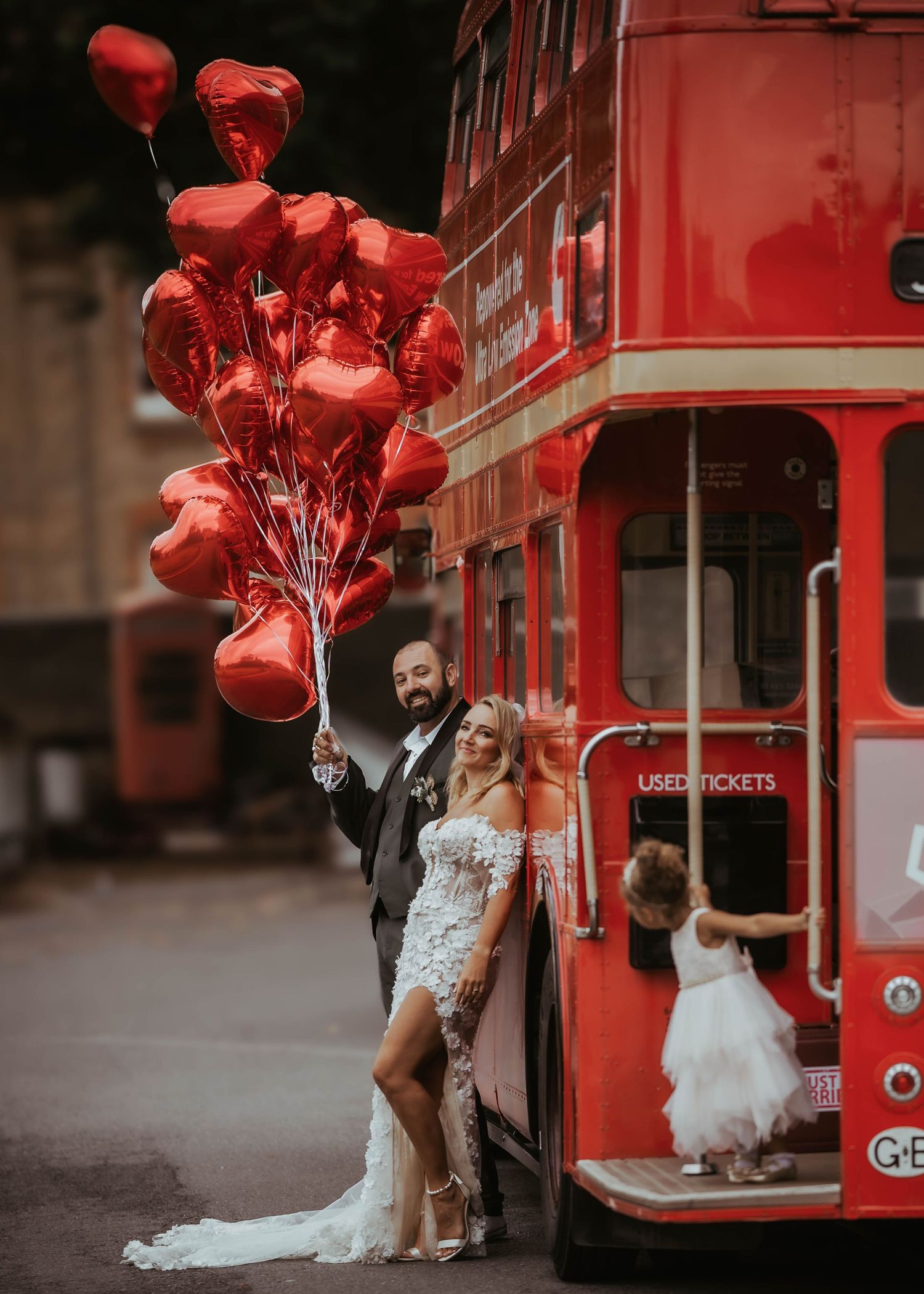 A romantic wedding photo with red heart balloons against a classic red double-decker bus.