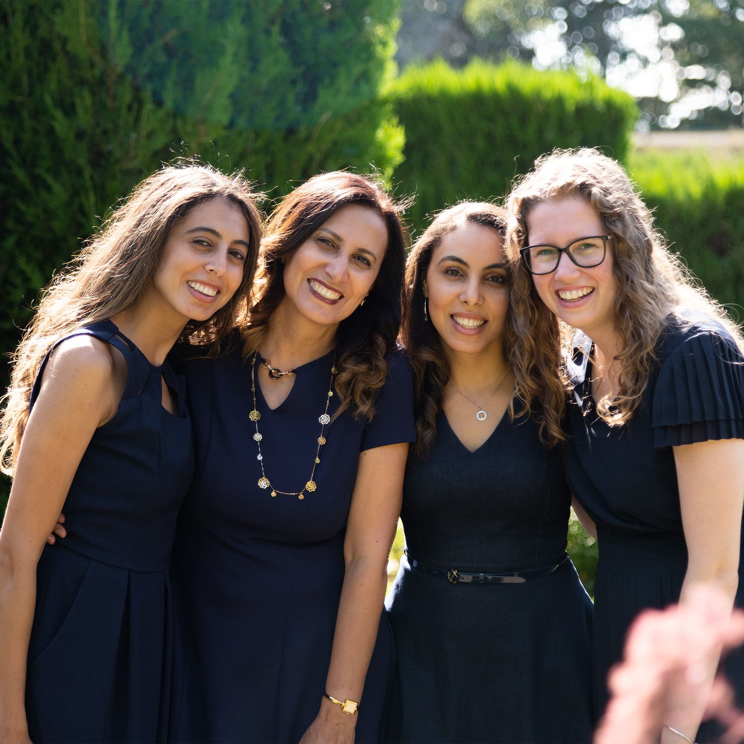 Group of four women wearing coordinating navy blue dresses pose in garden setting.