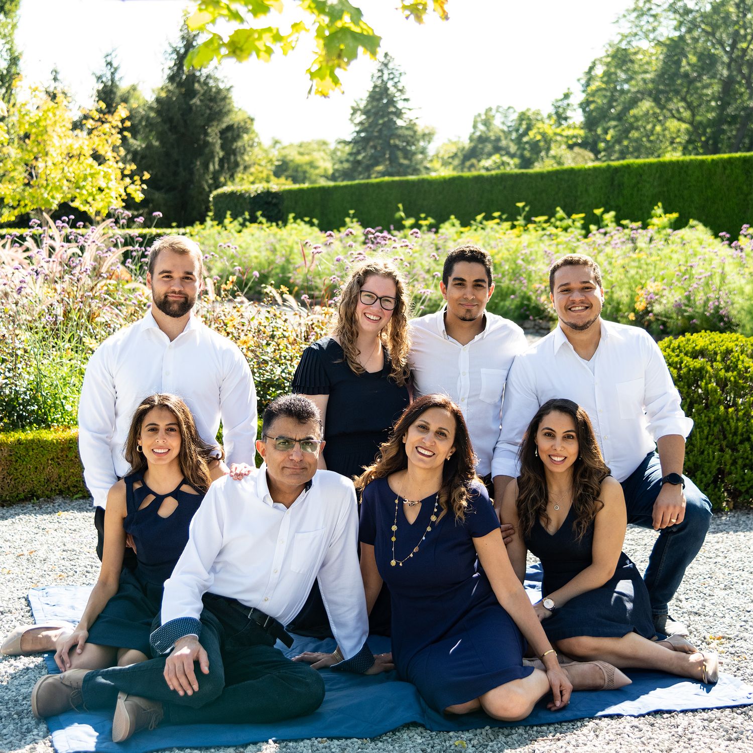 Family photo in coordinated navy and white outfits poses in blooming garden setting.