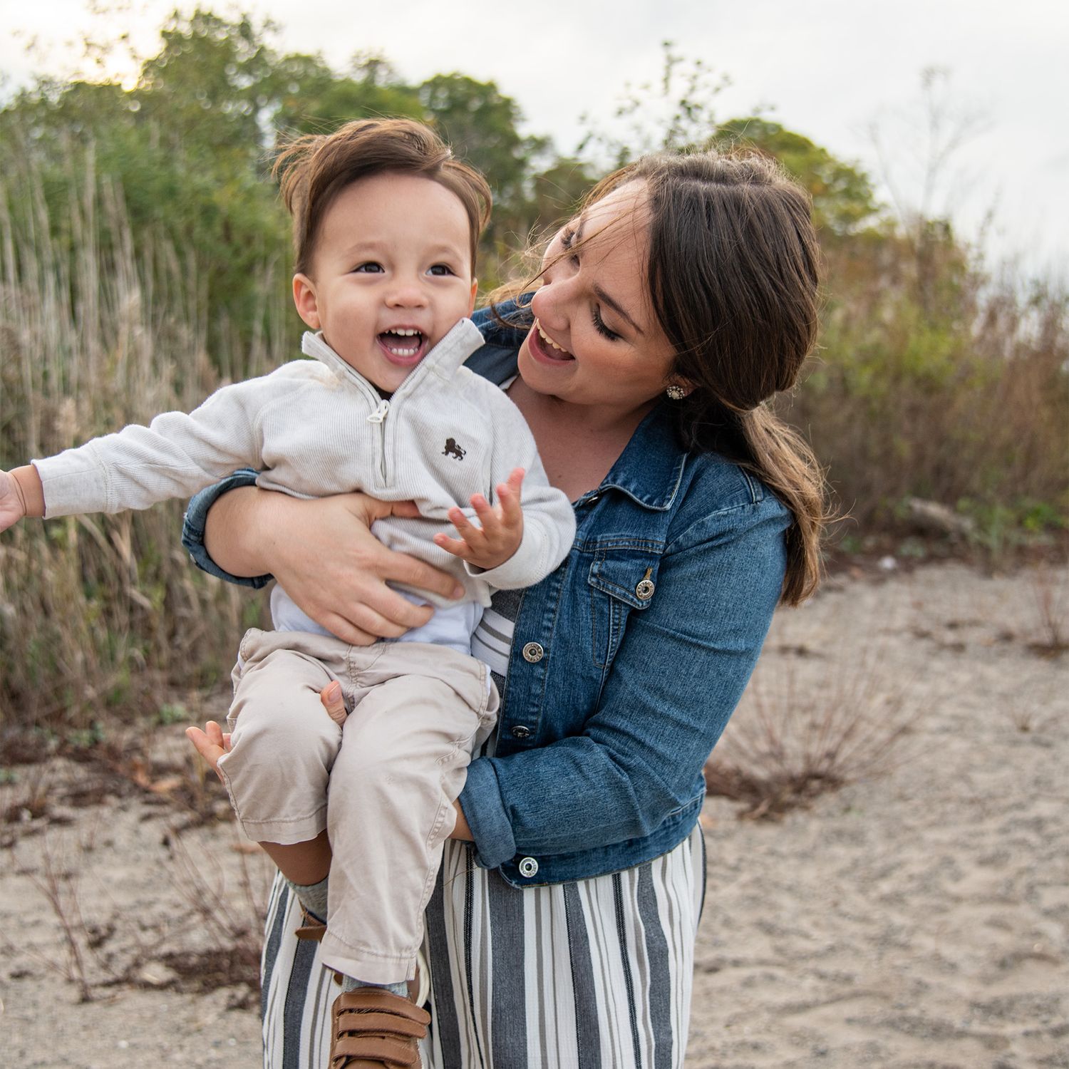 Candid moment of joy and laughter between parent and child in outdoor setting wearing denim and stripes.