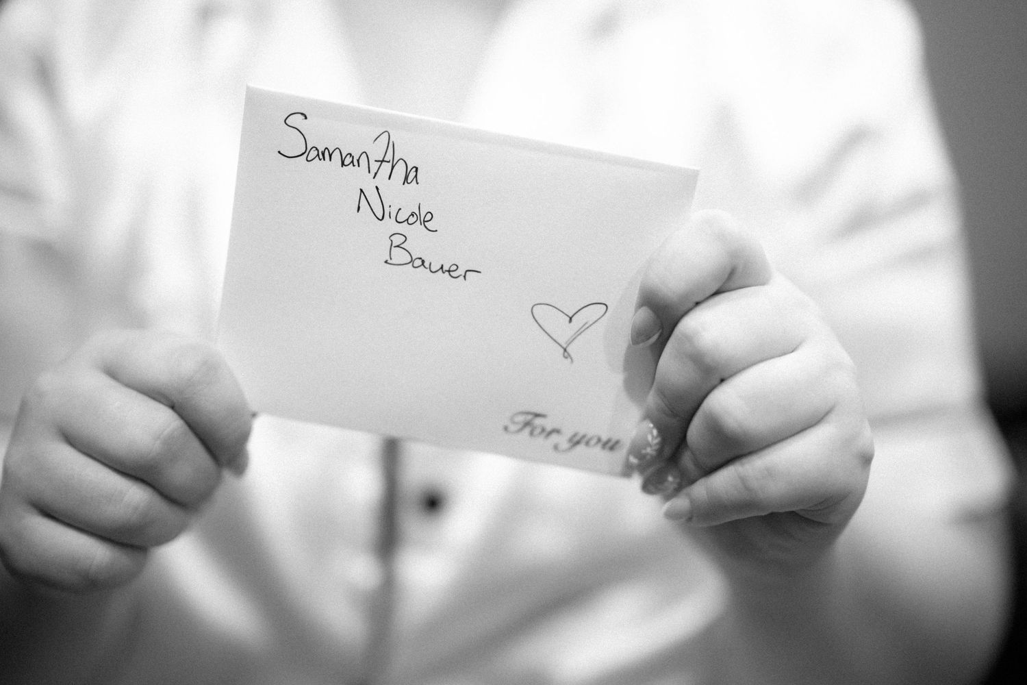 Hands hold a white envelope with writing and a heart drawn on it in black and white photography.