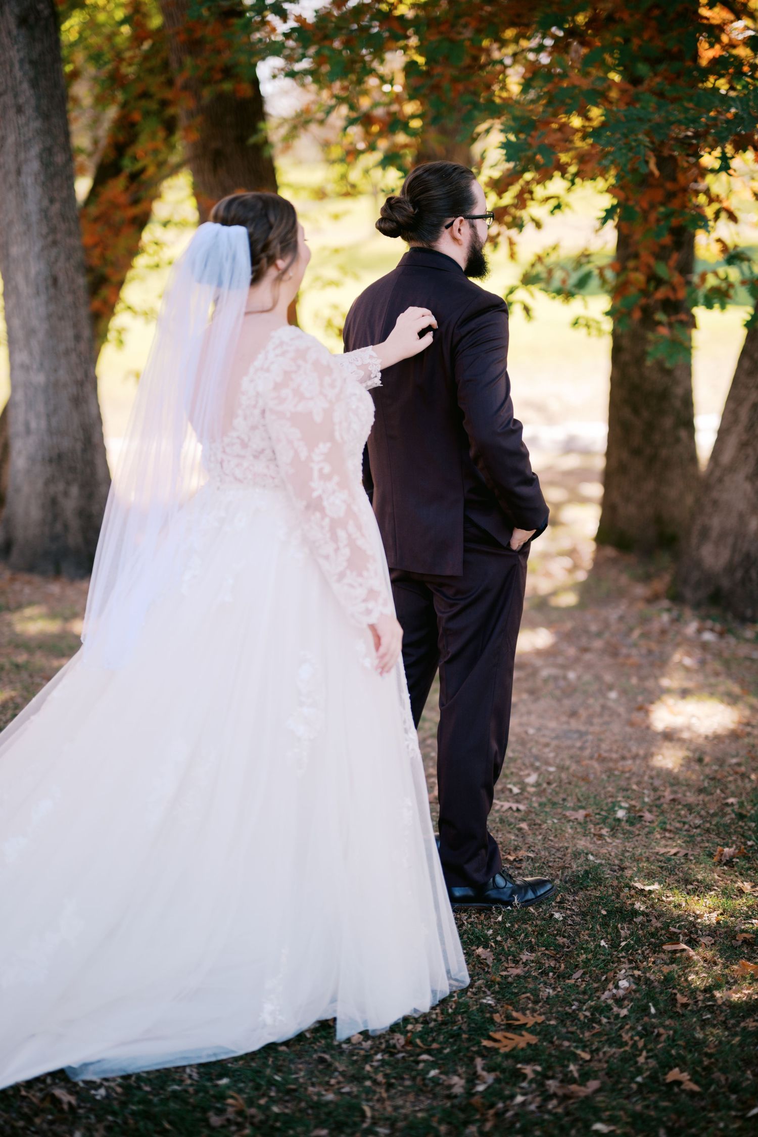 Bride and groom share private first look moment among fall trees.
