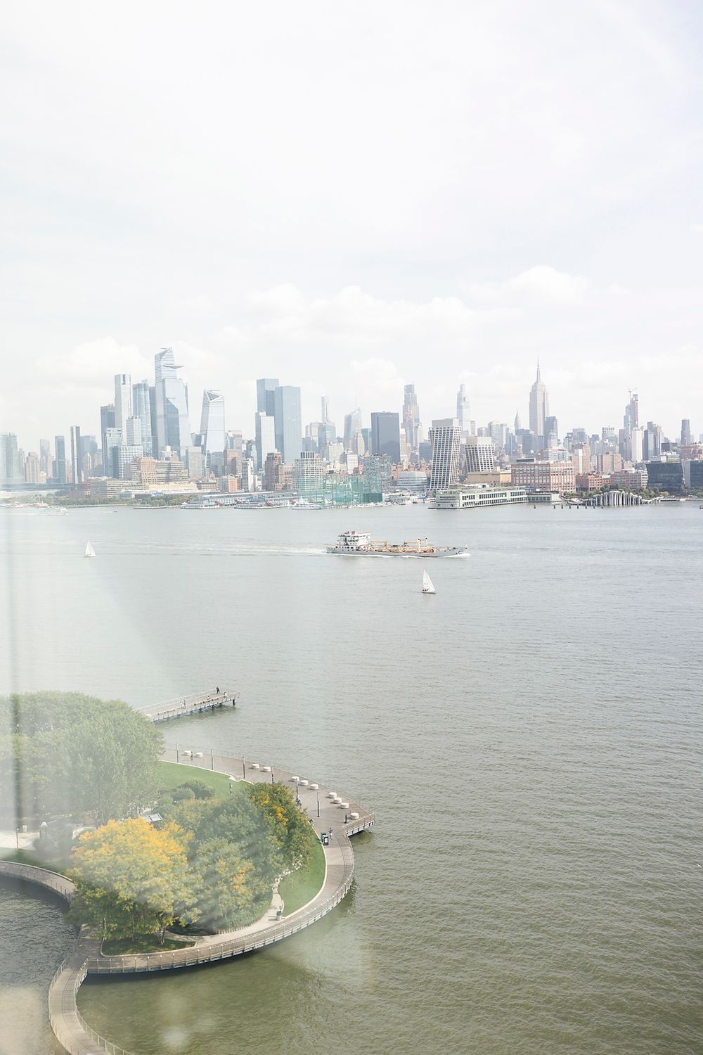 Aerial view of Manhattan skyline and Hudson River with curved walkway and greenery in foreground.