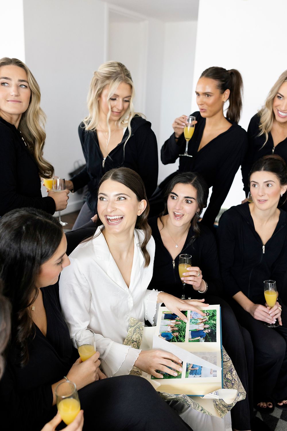 A group of friends in black and white attire gather together for drinks and laughter while looking at photos.