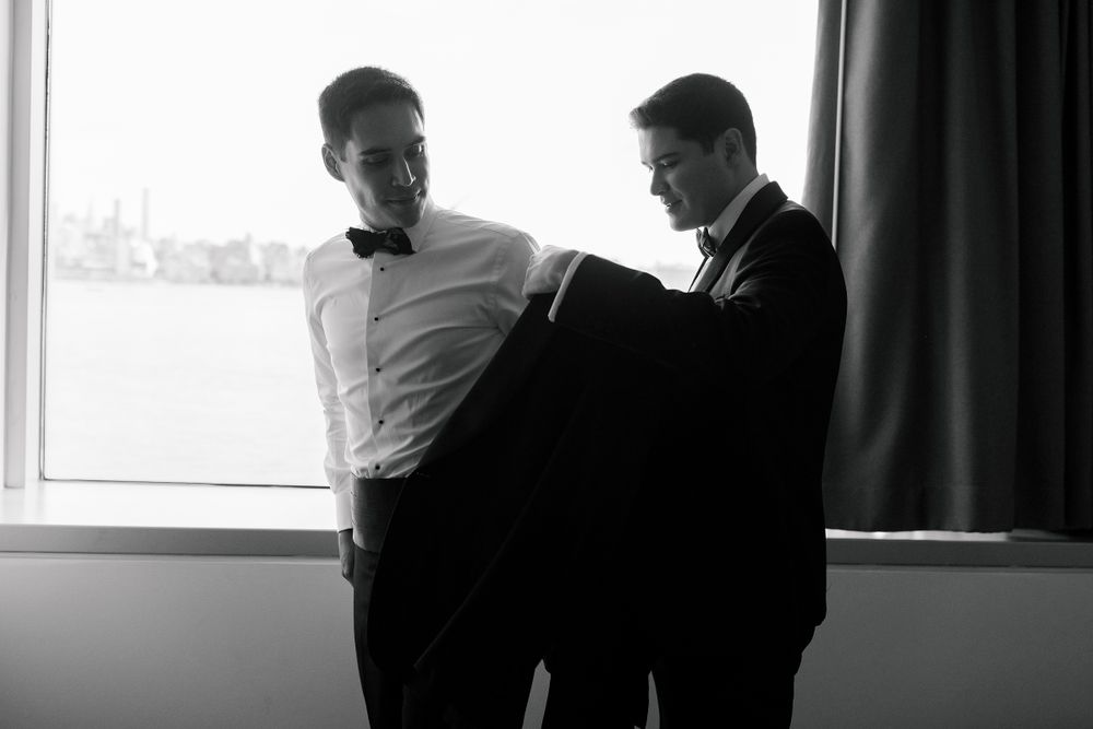 Two people in formal attire stand in conversation by a window in black and white photograph.