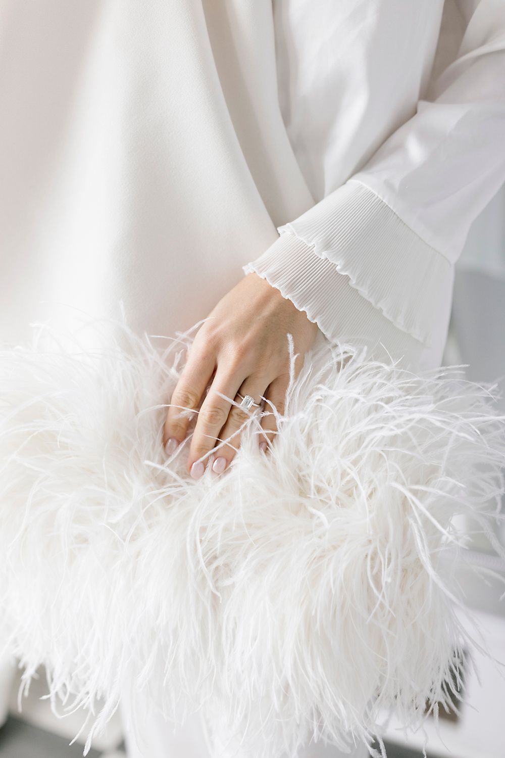 Elegant white feathered sleeve cuff detail with delicate ruffles and a ring adorned hand against soft fabric.
