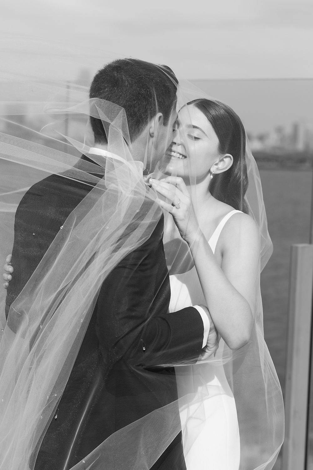 A romantic black and white wedding photo showing a couple embracing under a flowing veil on their special day.
