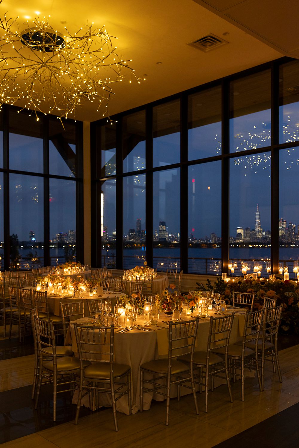 Romantic candlelit reception tables overlook Manhattan skyline through floor-to-ceiling windows with twinkling lights overhead.