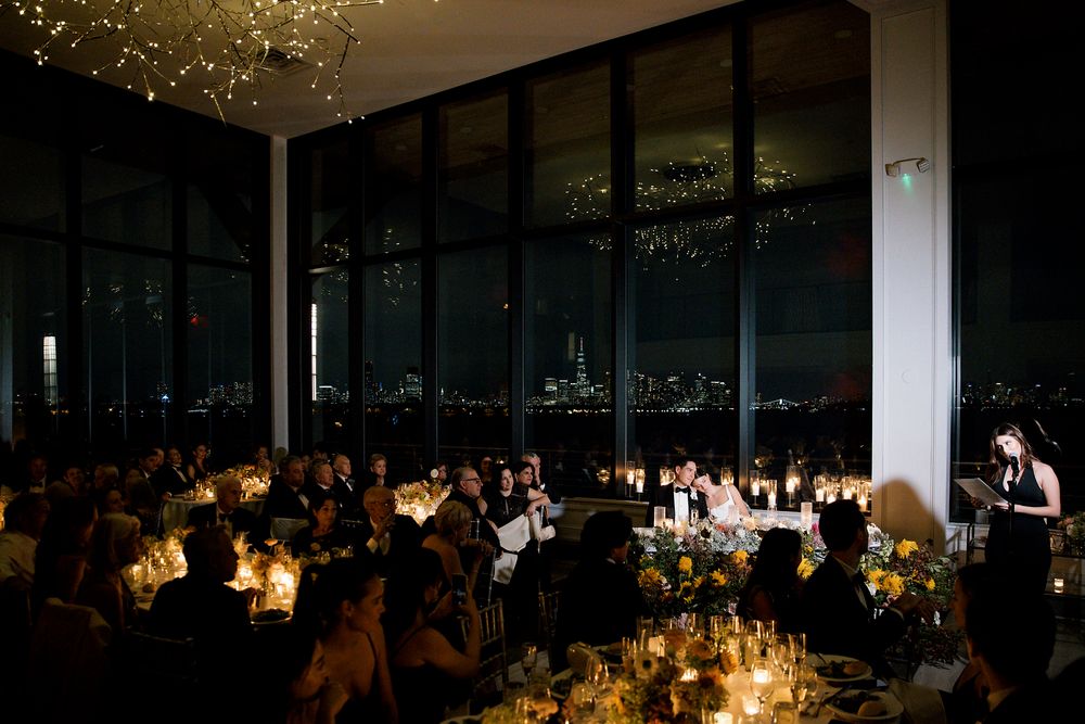 Candlelit wedding reception in a modern venue with floor-to-ceiling windows and guests seated at illuminated tables.