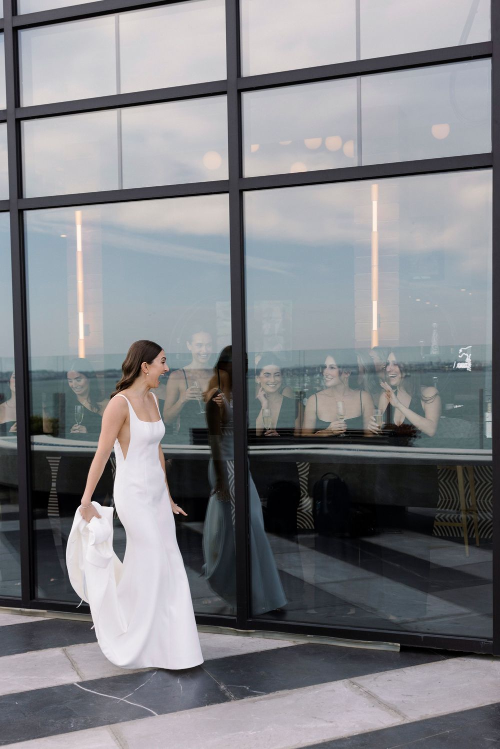 Person in elegant white maxi dress walking past modern glass building exterior with reflective windows.