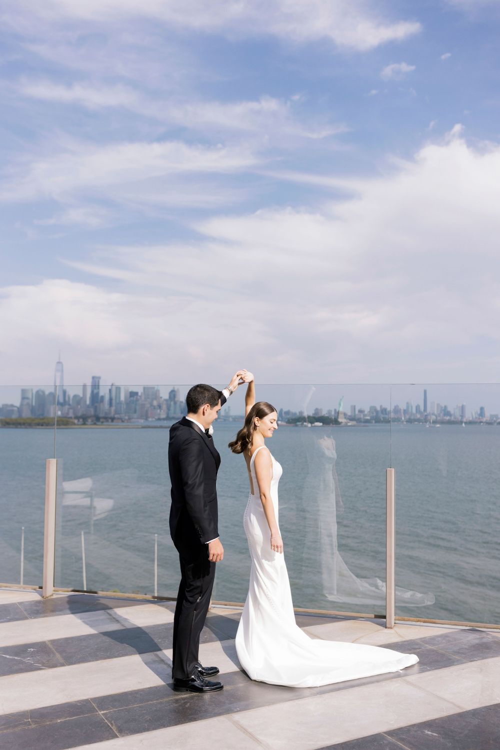Newlyweds share a romantic moment on a waterfront terrace with Manhattan skyline in the background.