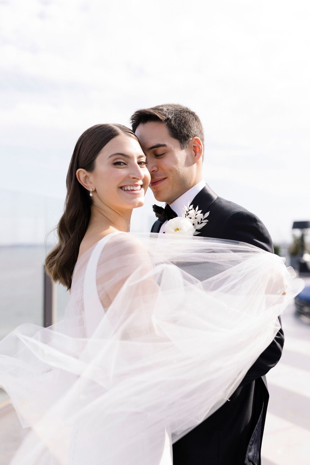A romantic wedding moment with the bride's veil flowing in the wind while the couple embraces.
