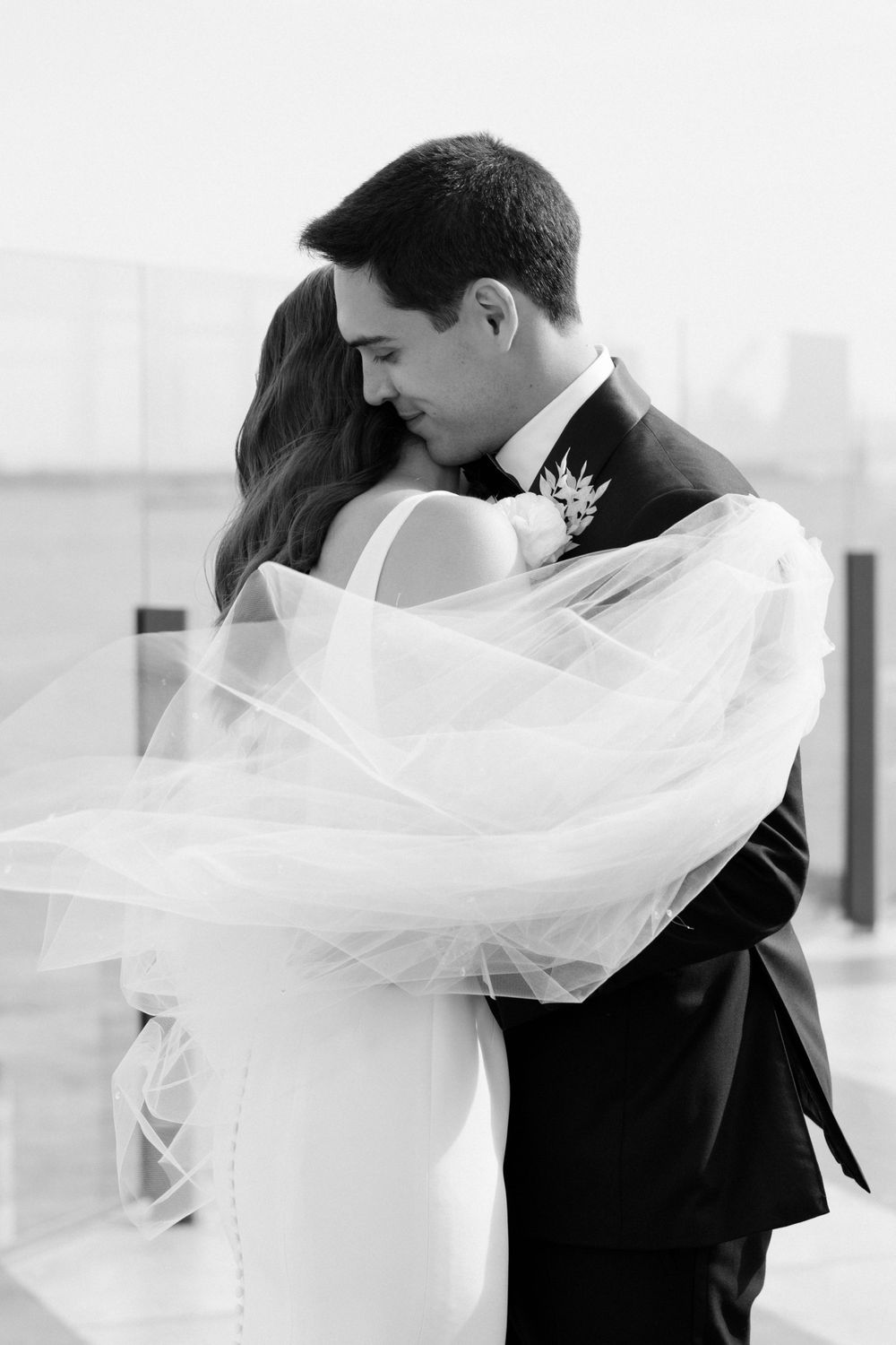 A romantic black and white wedding photo showing a tender moment as the bride's veil flows in the wind.