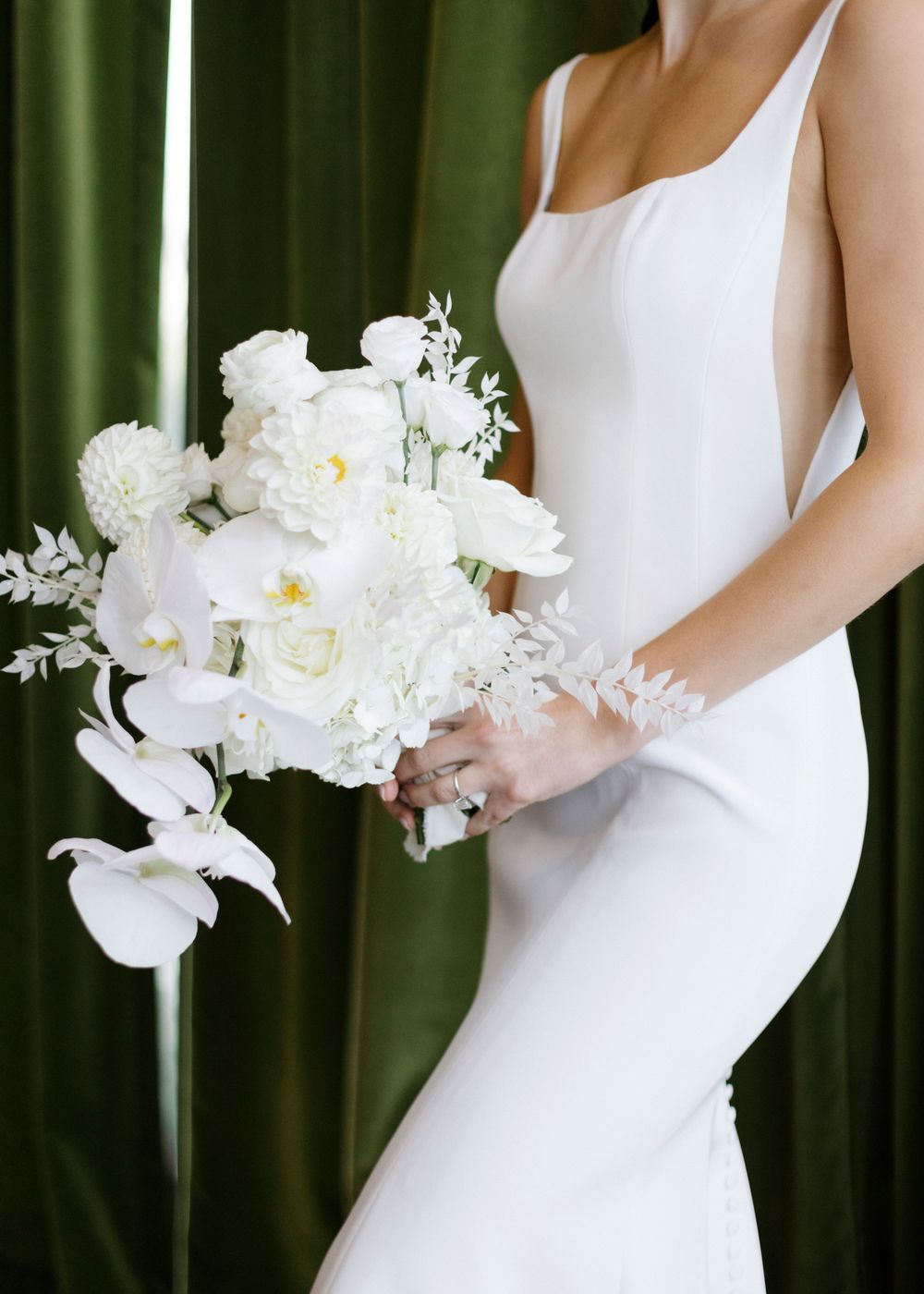 Elegant white bridal bouquet with roses and lilies held against a sleek form-fitting wedding dress.