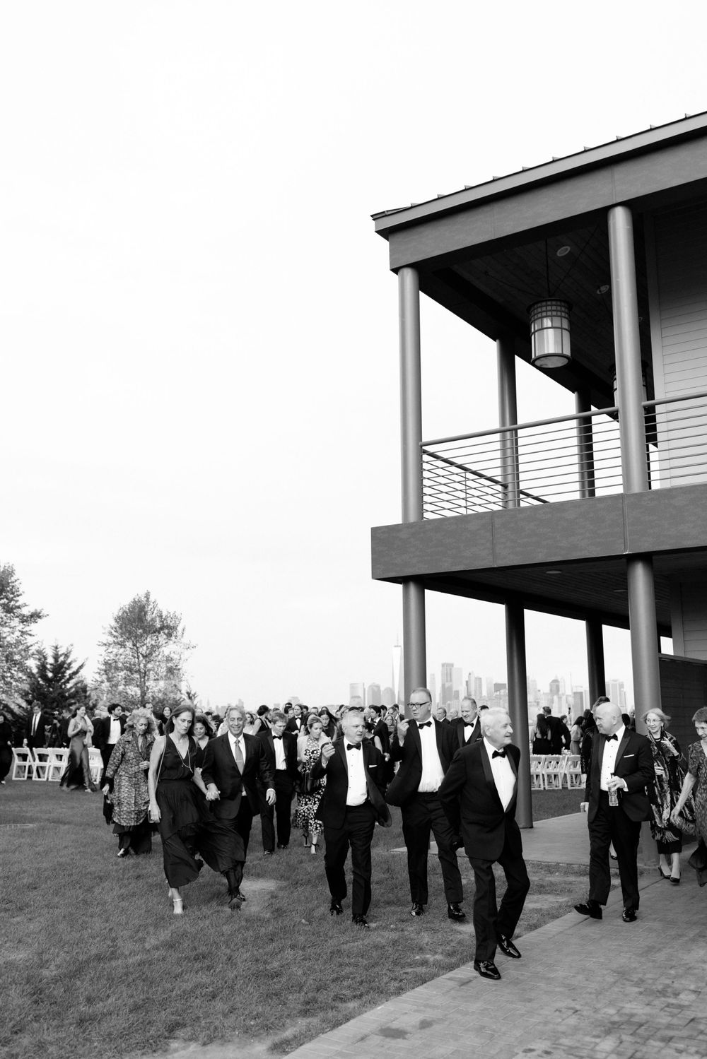 A black and white photo showing a large group of formally dressed guests walking outside a building at an event.