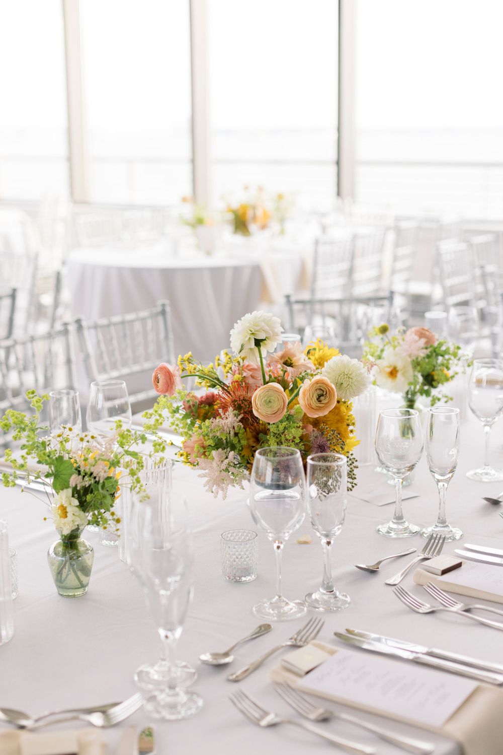 Elegant wedding reception table with white linens, silver chiavari chairs, and peach and yellow floral centerpieces.