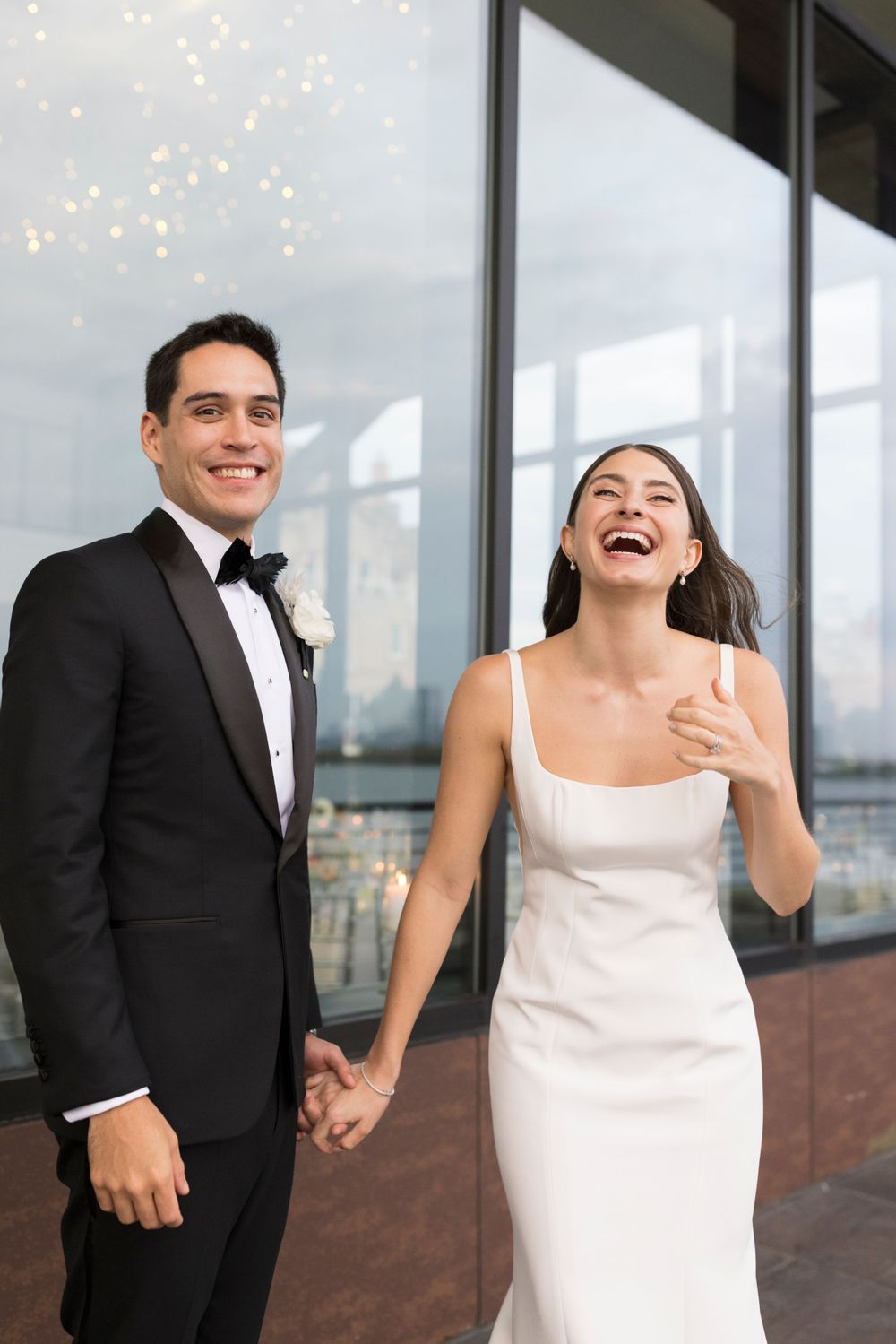 A joyful couple enjoying a candid moment together while dressed in wedding attire on a balcony.