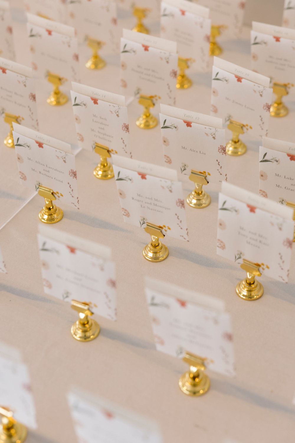 Wedding escort cards displayed with gold bell holders in neat rows on a light surface.