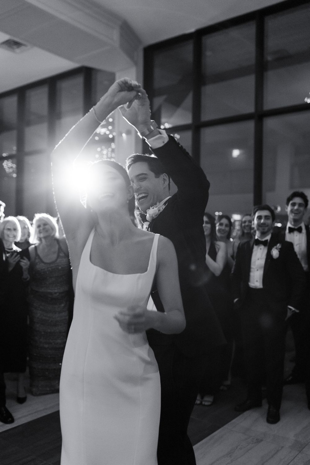 A couple sharing their first dance as newlyweds at an elegant wedding reception while guests watch in black and white.