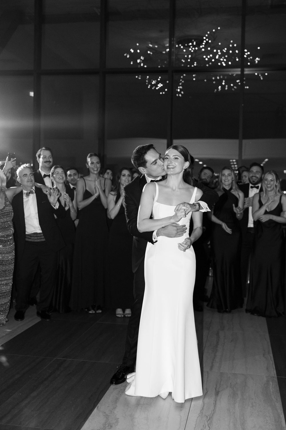 A couple shares their first dance at a wedding reception while guests watch and applaud in the background.