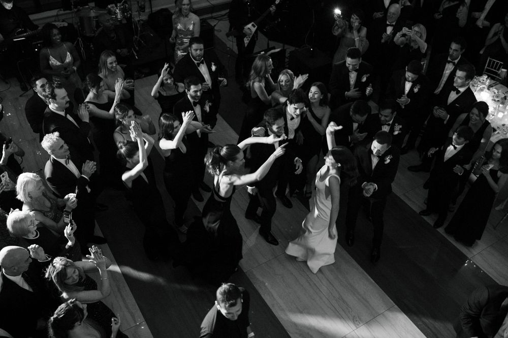 An overhead black and white shot of wedding guests dancing on a ballroom floor during a reception celebration.