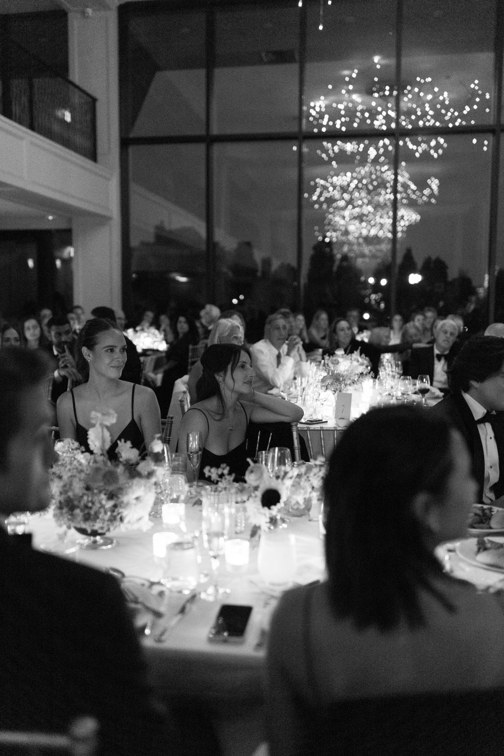 Elegant black and white wedding reception with candlelit tables and a sparkling chandelier in a grand windowed venue.