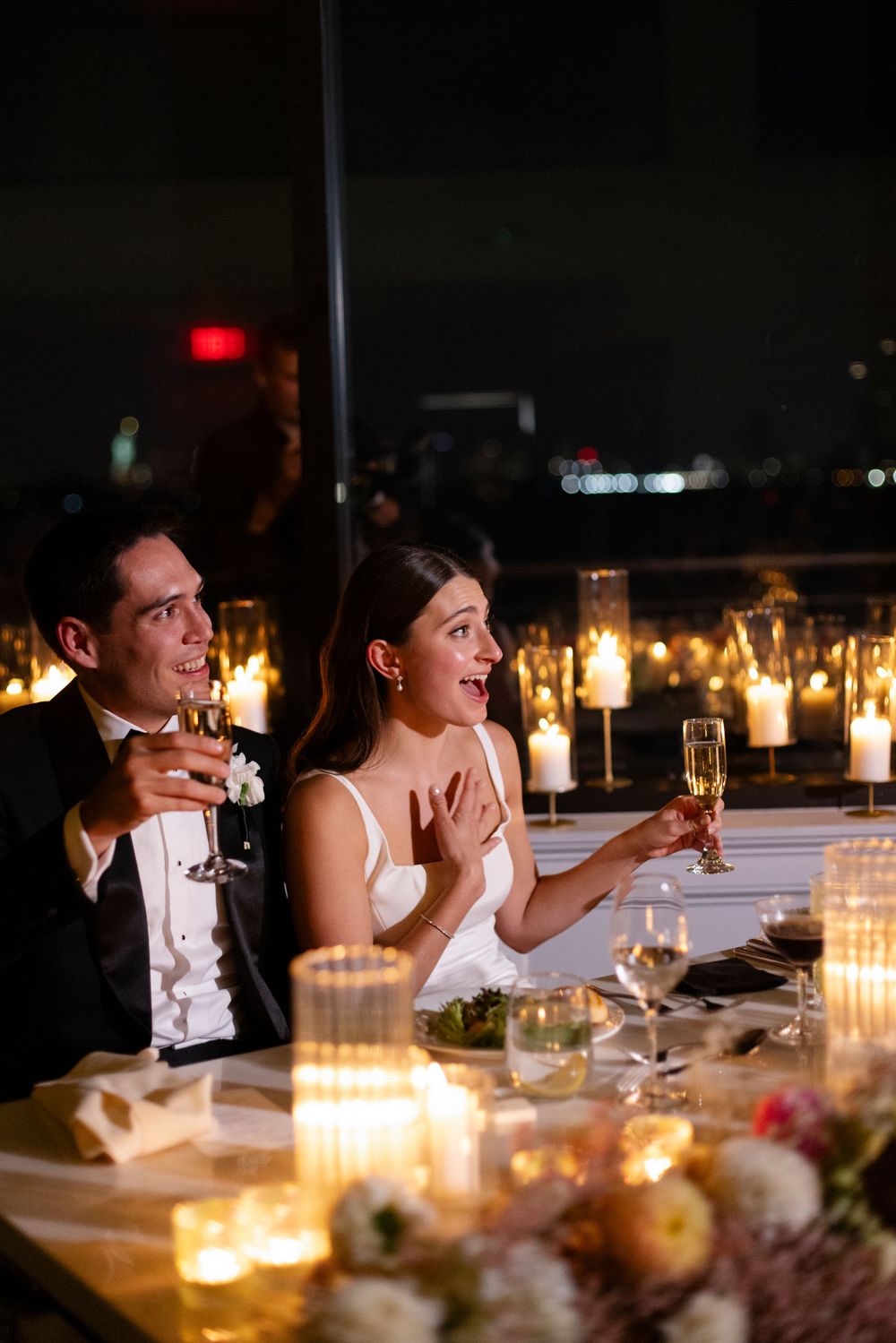 Couple enjoying candlelit dinner at elegant reception with champagne and glowing ambiance.