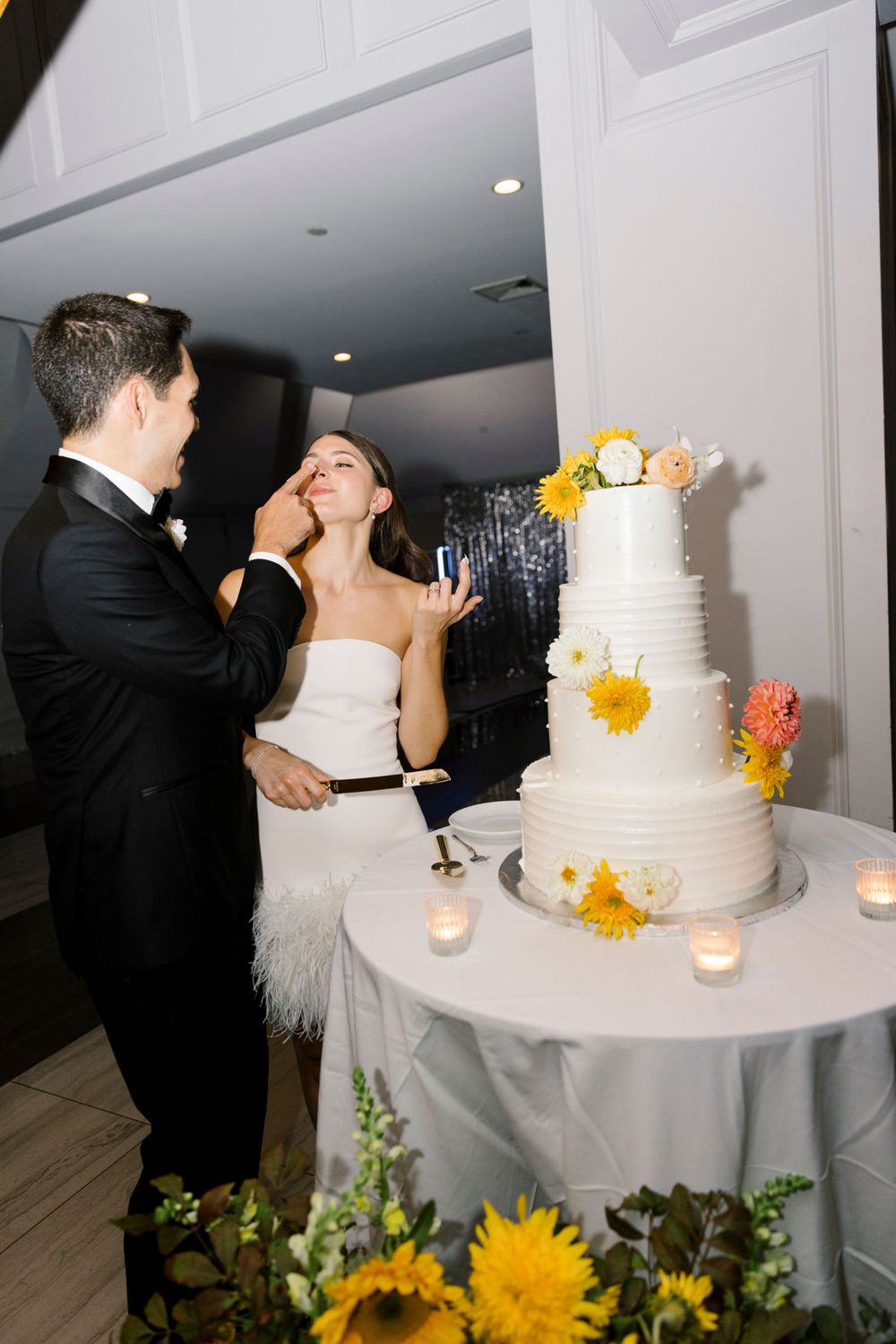 A classic wedding cake cutting moment with a white tiered cake decorated with yellow and peach flowers.