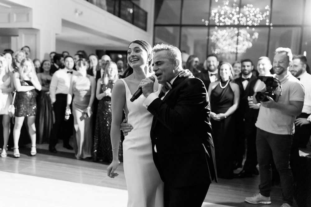 Joyful couple dancing at their wedding reception in a sleek venue with onlooking guests in black and white photography.