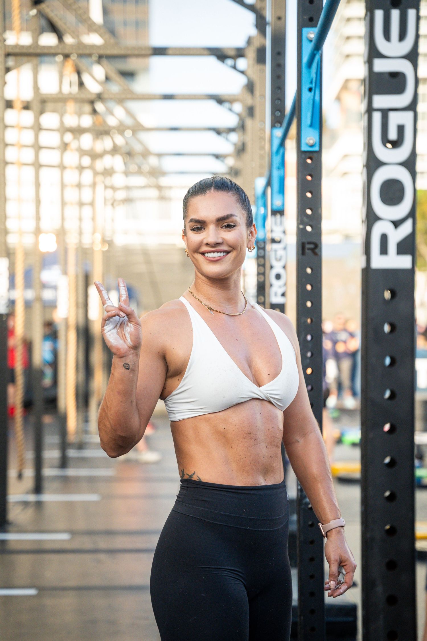 Athlete showing peace sign at CrossFit gym with Rogue equipment in background.