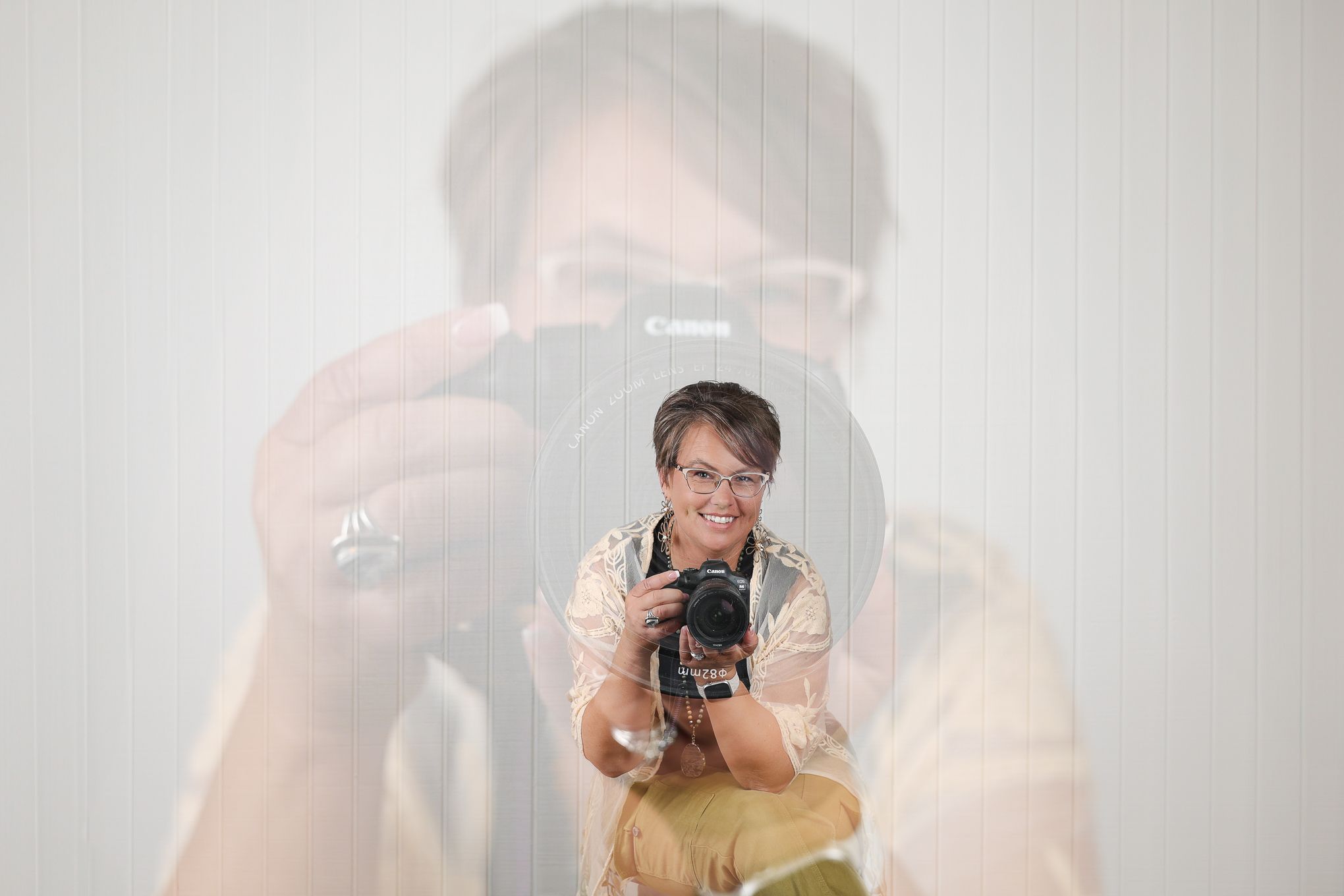 A photographer taking a self-portrait in the mirror while holding a camera with soft lighting.