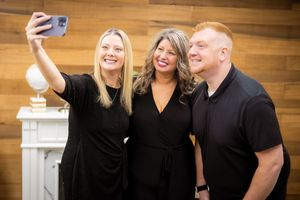 A group of people dressed in black laugh together in a candid photo series against a wood-paneled wall.