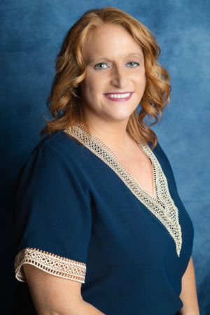 Professional studio portrait against blue background wearing navy dress with white lace trim.