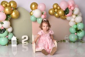 Birthday celebration setup with pink, mint and gold balloon arch and number decorations.