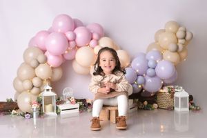Elegant cake photoshoot setup with blush pink and beige balloon garland against neutral backdrop.