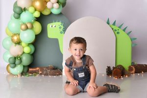 Dinosaur themed photo session with green balloon arch and prehistoric decorations.