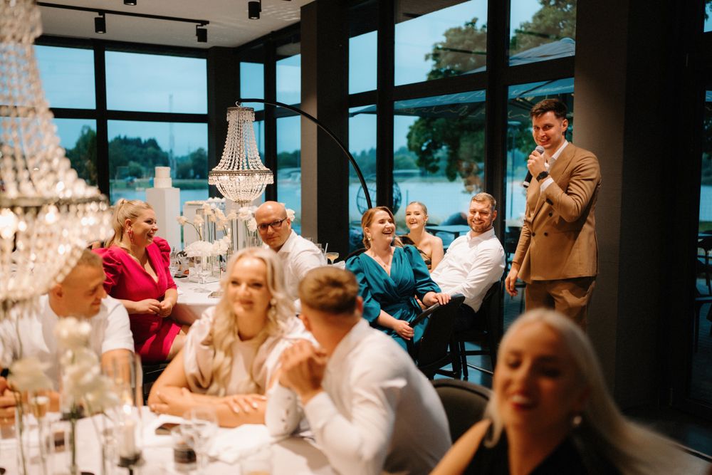 Wedding reception guests seated at elegantly decorated tables with crystal chandeliers overhead.