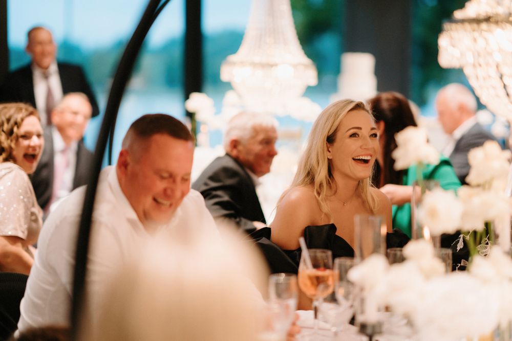 Wedding celebration with guests dining under crystal chandeliers in natural lighting.
