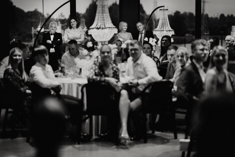 Black and white panorama of wedding guests seated at round tables during a reception celebration.