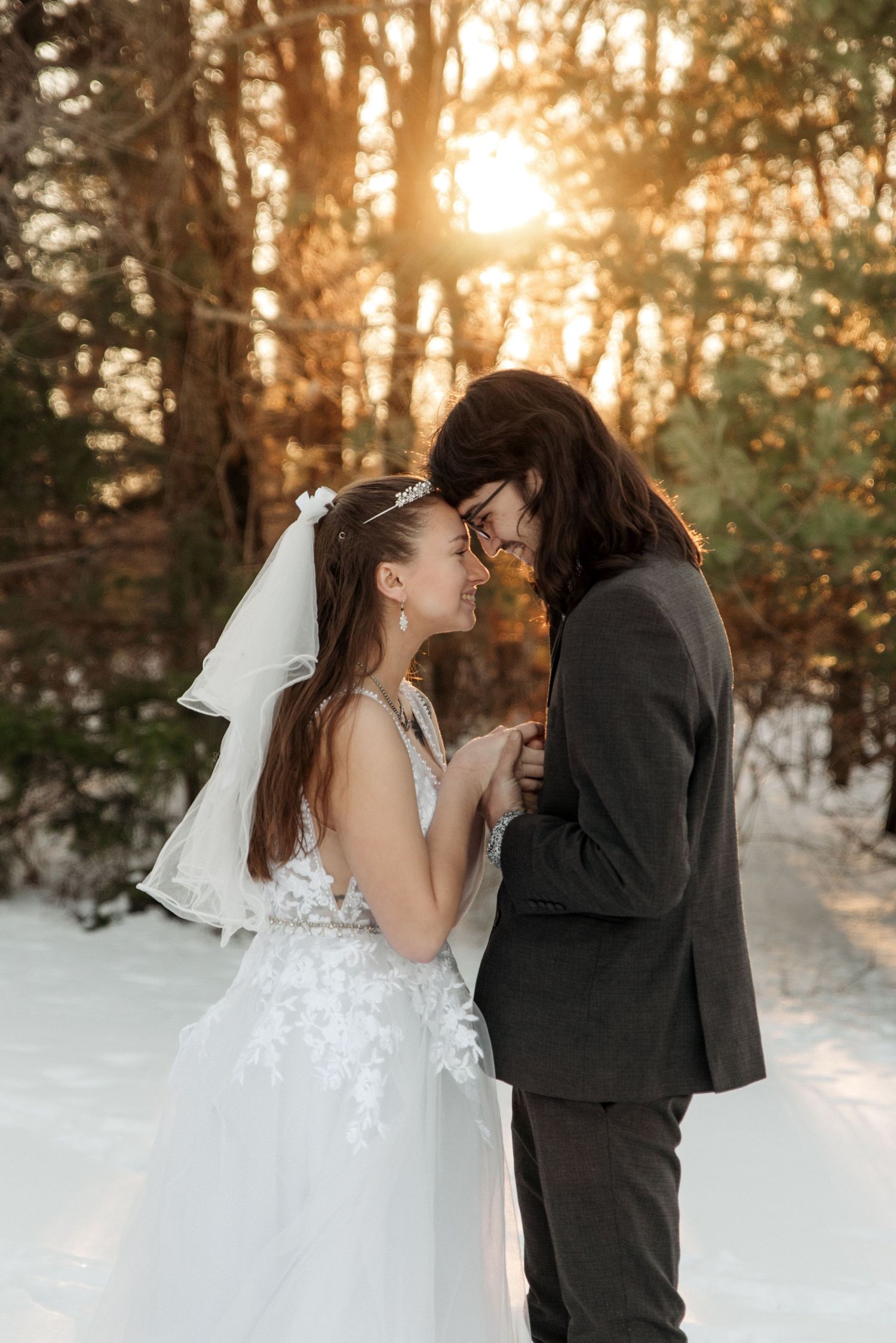 Romantic winter wedding photo with sunlight filtering through snowy trees.