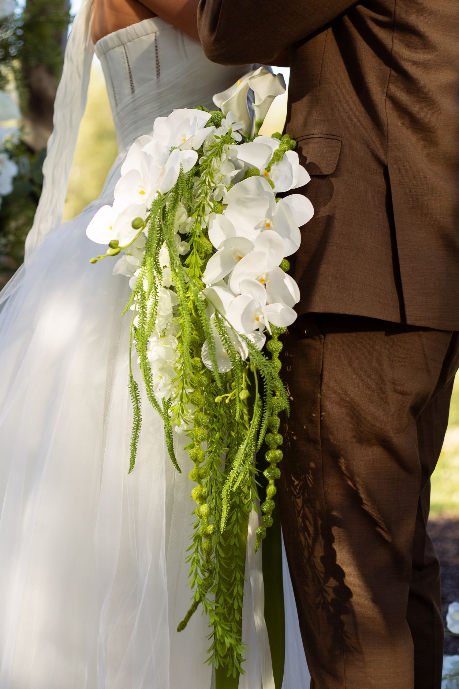White orchids and cascading green amaranthus create an elegant wedding bouquet detail.