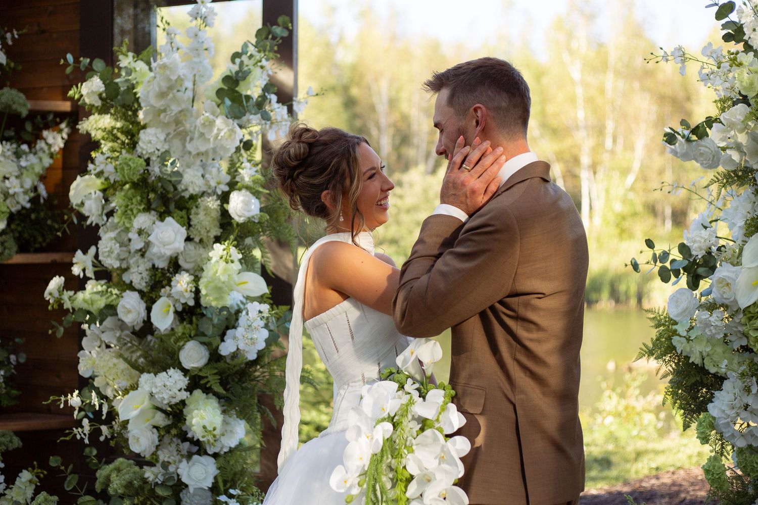 A romantic wedding ceremony scene with white floral arch decorations and natural lighting.