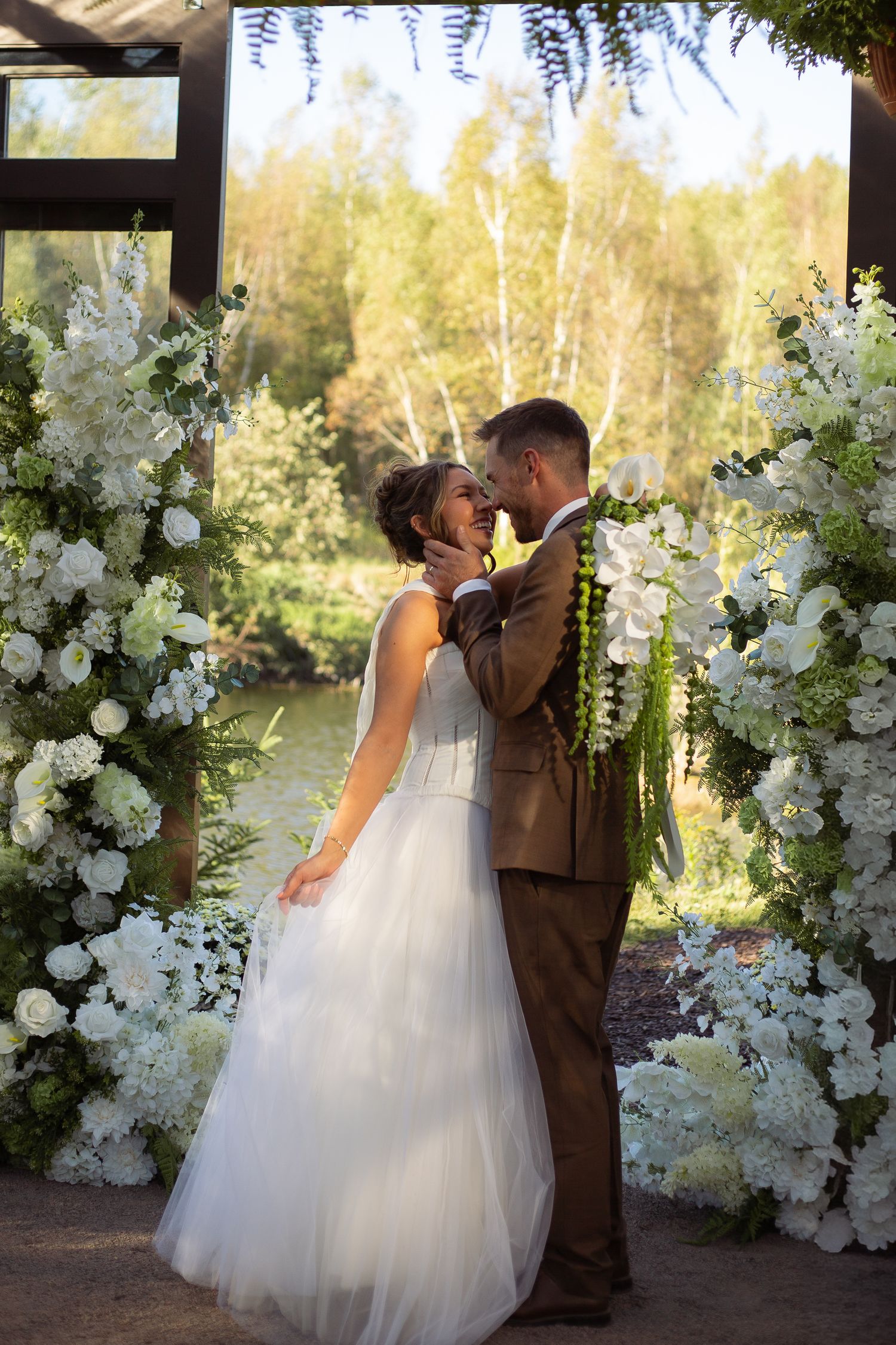 A romantic wedding photo sequence with a couple kissing against a backdrop of white floral arrangements and trees at sunset.